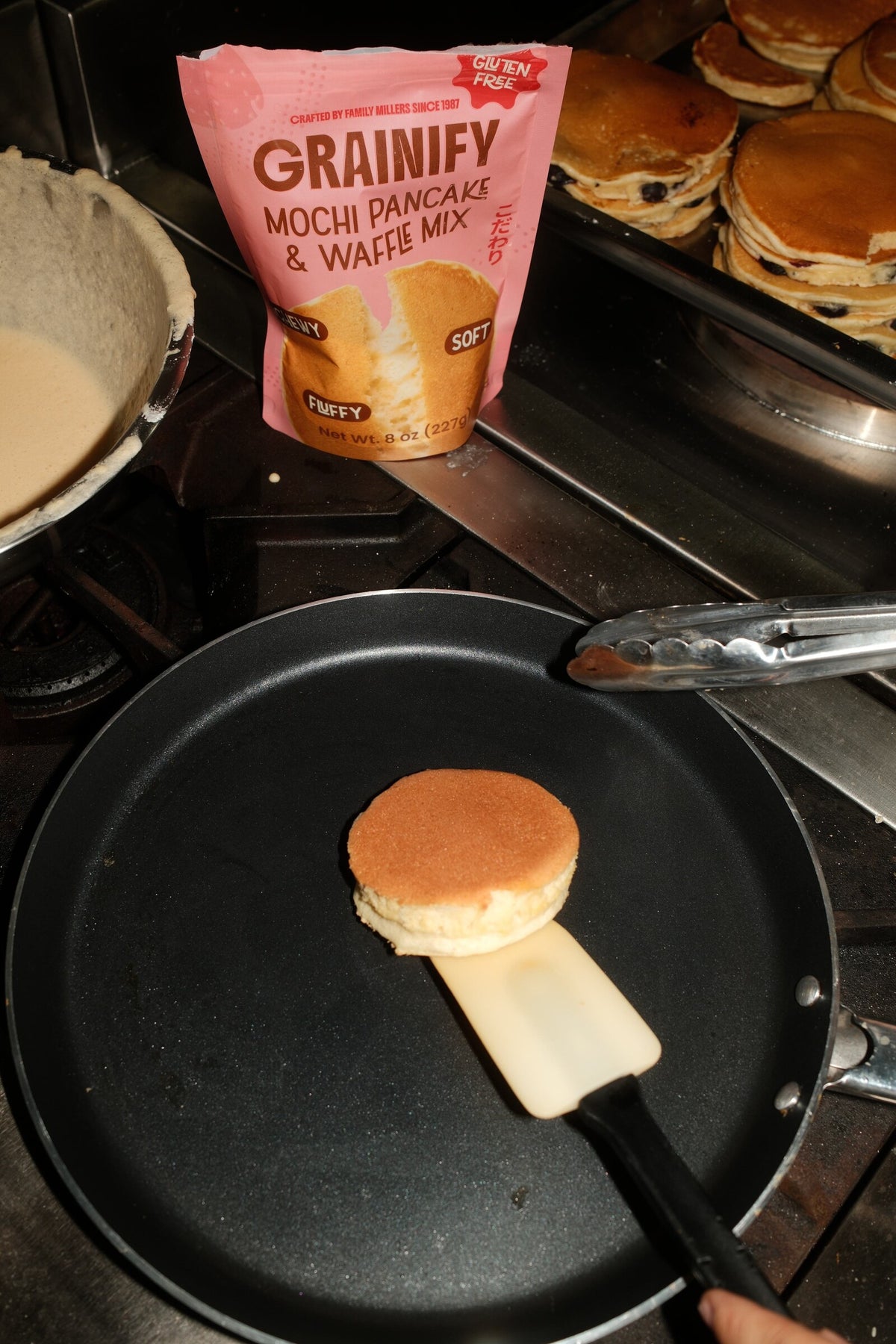 Mochi pancake cooking on a griddle next to the Grainify mix pouch