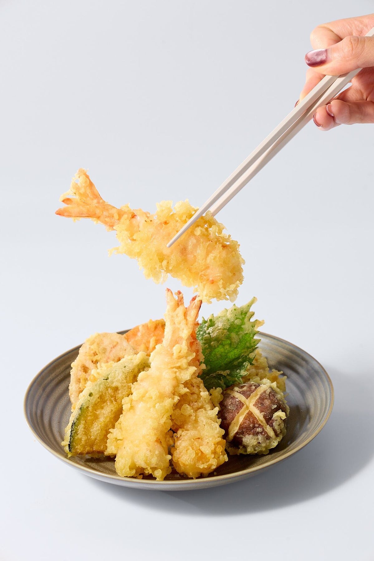 Crispy shrimp tempura lifted with chopsticks over a bowl of tempura